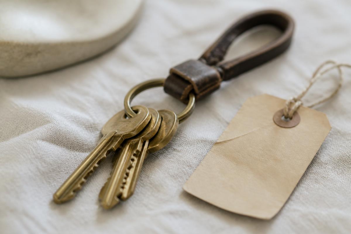 Brass house keys on a leather keyring beside a paper luggage tag